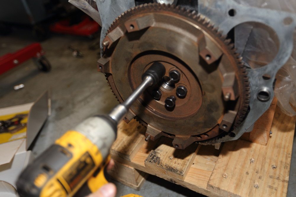 Start the flywheel bolts by hand, then run them in with an impact gun. No need to hammer them in with the impact. You’re going to tighten them using a torque wrench. 
